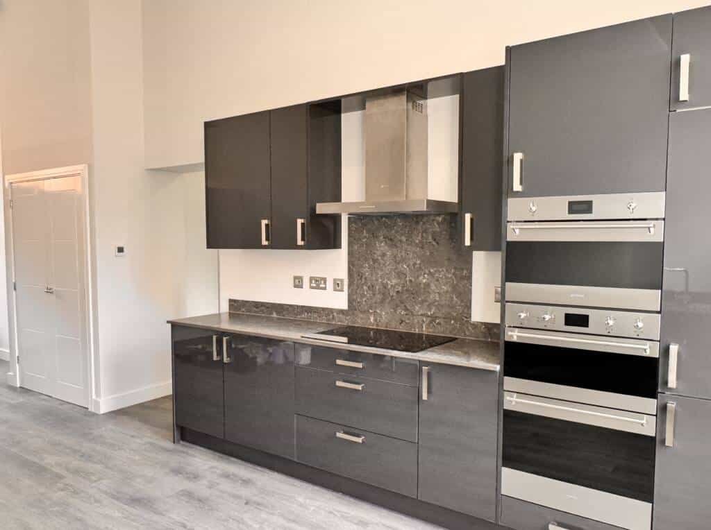 Contemporary high-gloss charcoal grey bespoke kitchen furniture featuring integrated double ovens and a minimalist stainless steel extractor hood.