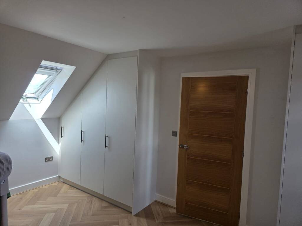 Custom-built white wardrobes designed to fit perfectly under a sloped attic ceiling with a skylight.