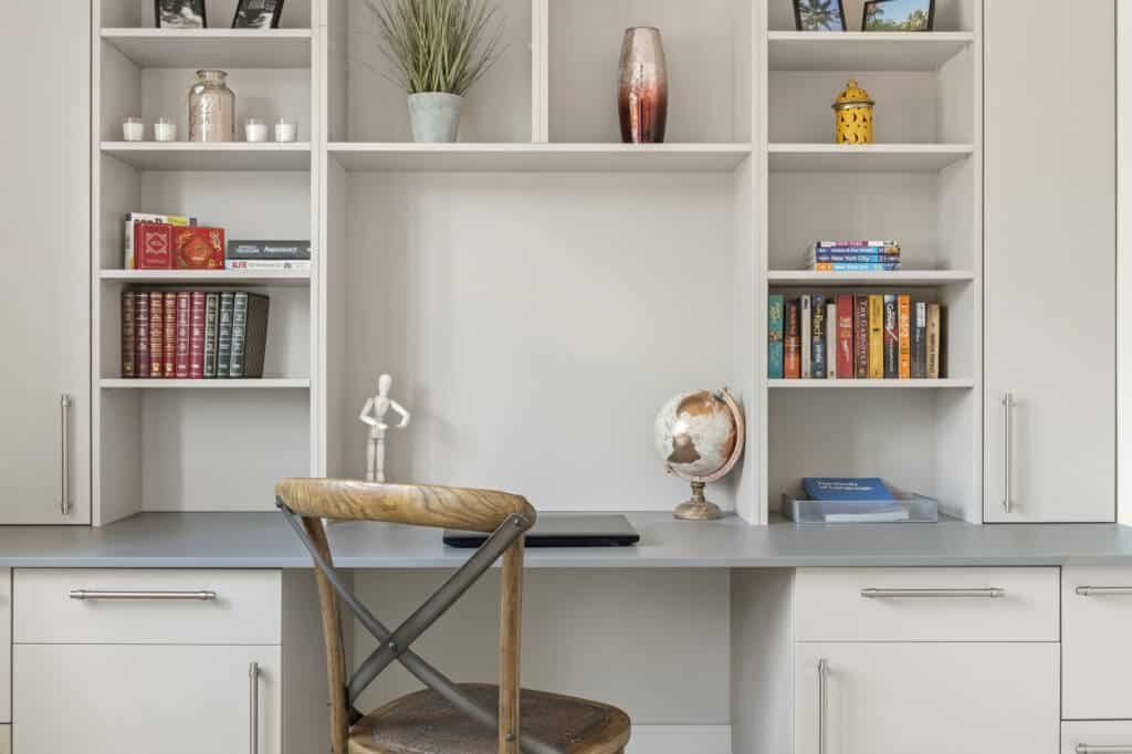 Modern bespoke fitted study furniture in light grey featuring a built-in desk, open bookshelves, and sleek storage cabinets.