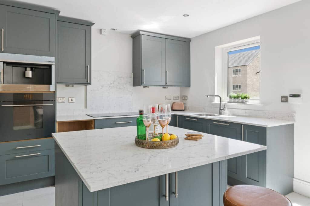 Bright and modern bespoke kitchen furniture in slate blue featuring a large white marble-topped island and integrated high-end appliances.