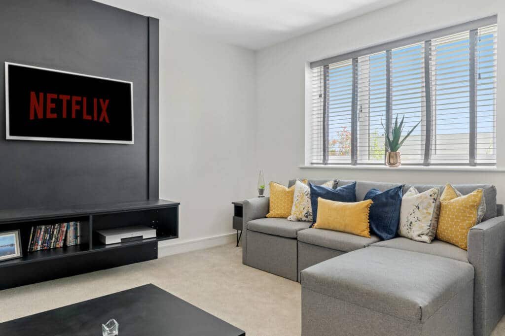 Modern living room with dark grey media wall unit, wall-mounted TV displaying Netflix, and floating storage shelf beneath.