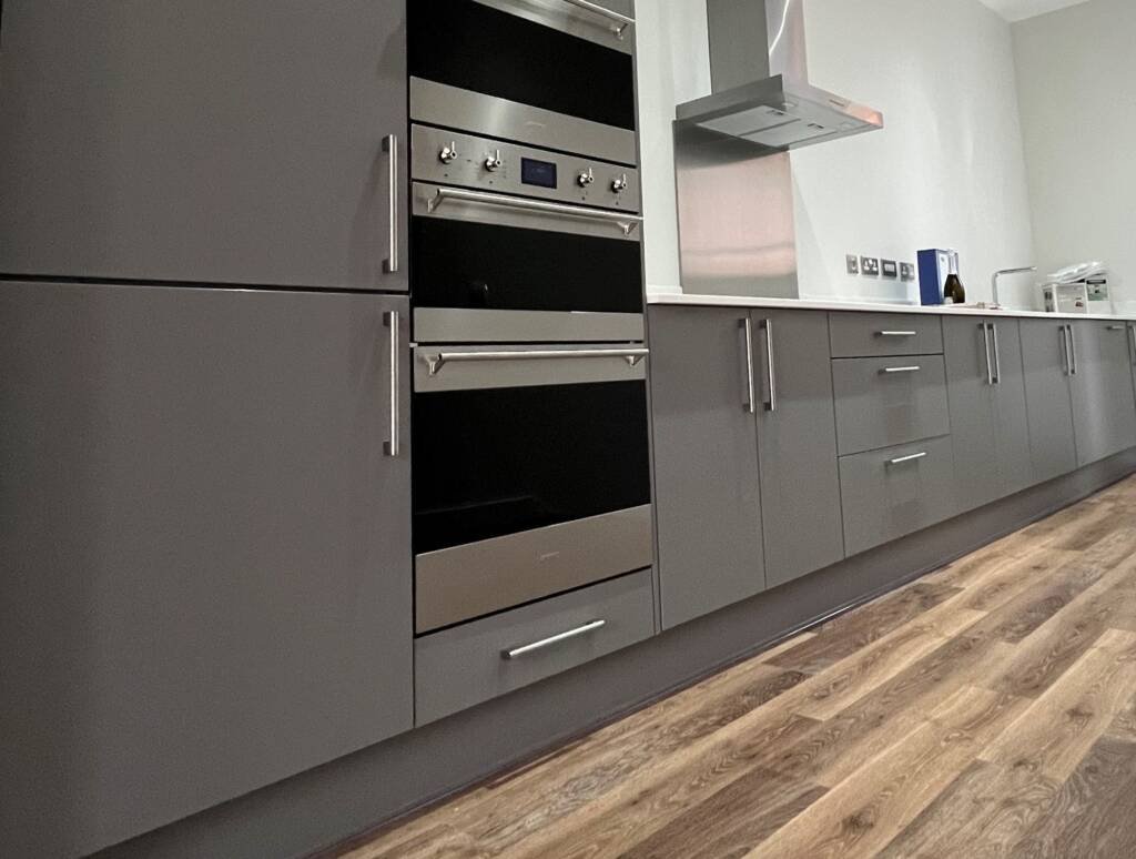 Modern graphite grey bespoke kitchen furniture featuring a seamless run of base cabinets and high-end integrated stainless steel double ovens.