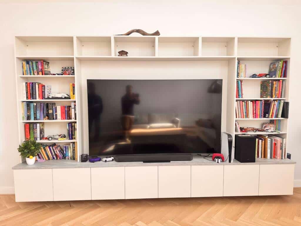 Contemporary living room with bespoke media wall unit featuring built-in shelving, large flat-screen TV, and integrated storage cabinets.
