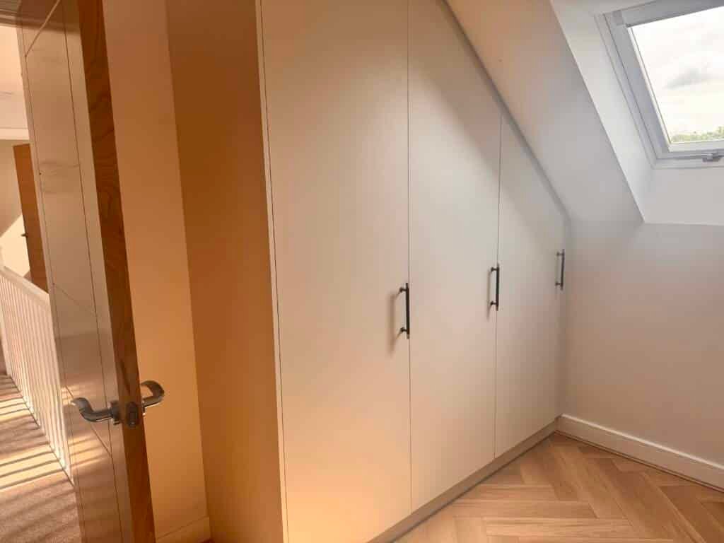 Custom white wardrobe design for sloped ceilings featuring minimalist handles and a precision-fit slanted top.