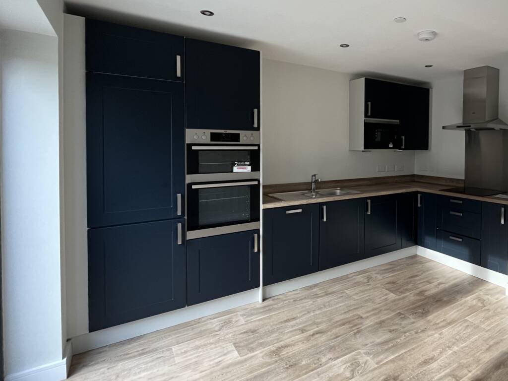 Navy blue Shaker-style bespoke kitchen furniture featuring light wood countertops, integrated stainless steel ovens, and a dual-basin sink.