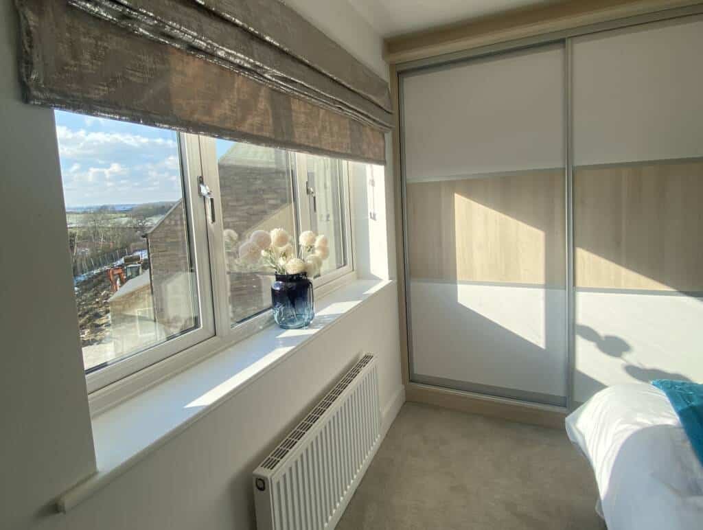 Bright bedroom featuring fitted wardrobes with white and light wood sliding doors next to a large window.