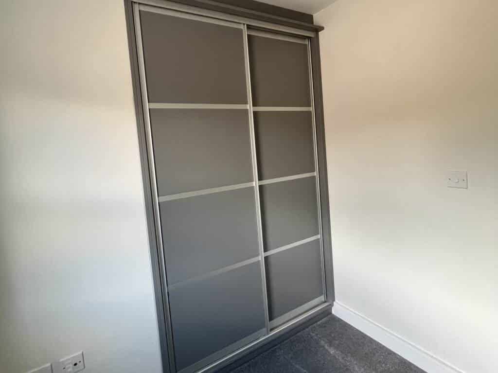 Minimalist grey fitted wardrobes with two sliding doors and a four-panel horizontal design in a modern bedroom.