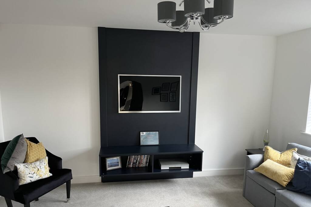 Minimalist living room with dark blue media wall unit, wall-mounted TV, and floating storage shelf.