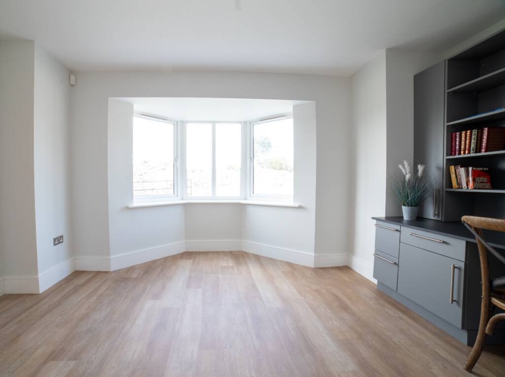 Modern grey fitted study furniture installed in a bright room with a large bay window and wood-effect flooring.