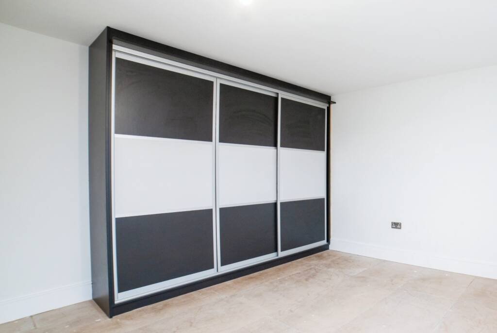 Modern three-door sliding fitted wardrobes with a black and white panel design in a minimalist room.