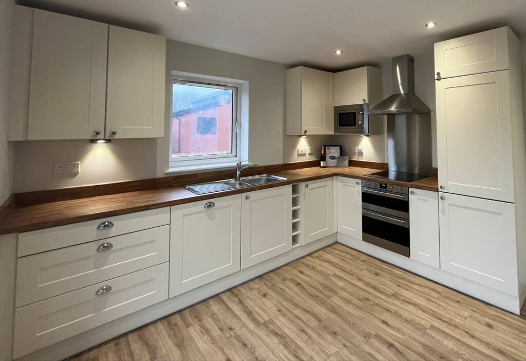 Elegant cream Shaker-style bespoke kitchen furniture featuring warm wood countertops, integrated appliances, and silver knob handles.