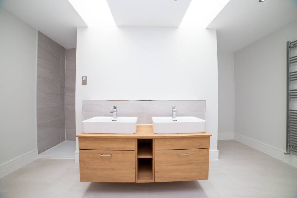Modern double vanity unit as part of a fitted bathroom furniture installation with a light oak finish and vessel sinks.