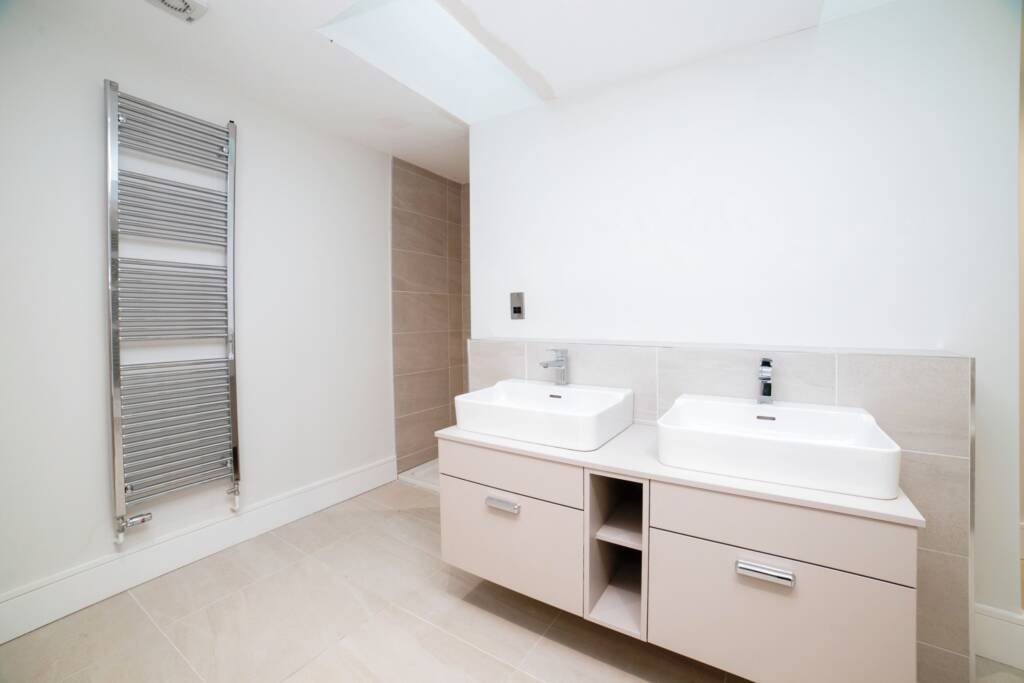 Contemporary fitted bathroom furniture featuring a light-colored floating double vanity with sleek metal handles and white rectangular basins.