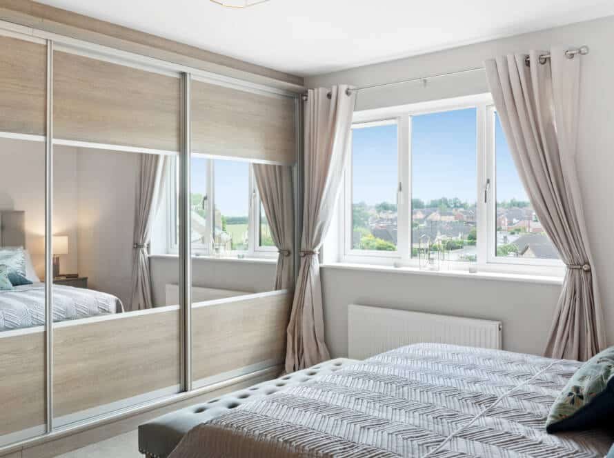 Elegant floor-to-ceiling wardrobe design featuring three sliding doors with large mirrored panels and a light wood finish in a master bedroom.