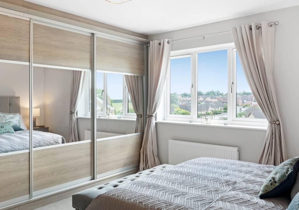 Elegant floor-to-ceiling wardrobe design featuring three sliding doors with large mirrored panels and a light wood finish in a master bedroom.